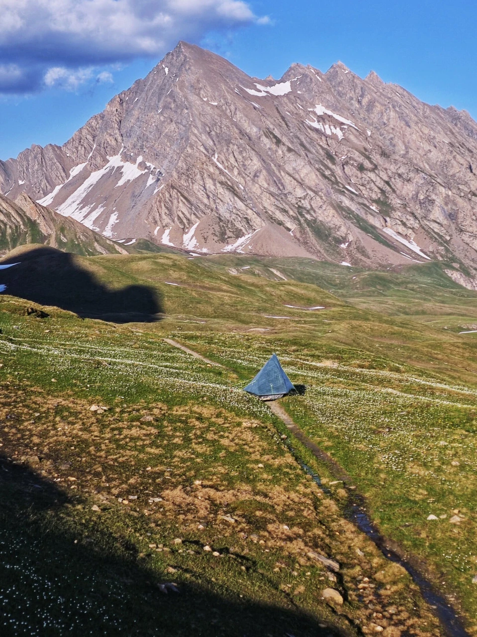 Tält uppsatt på en fjälläng på TMB i början av juni, pyttelitet under toppen med snön fortfarande kvar: en stämning som inte längre finns när högsäsongen är igång